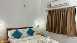 A neatly made bed with white and teal pillows, a wooden headboard, and a white bedside table with a small object on it. - The Blackbuck Ashwem (Ashvem)