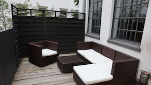 En patio med en mørk fletsofa og to lænestole, et lille bord og en træterrasse.