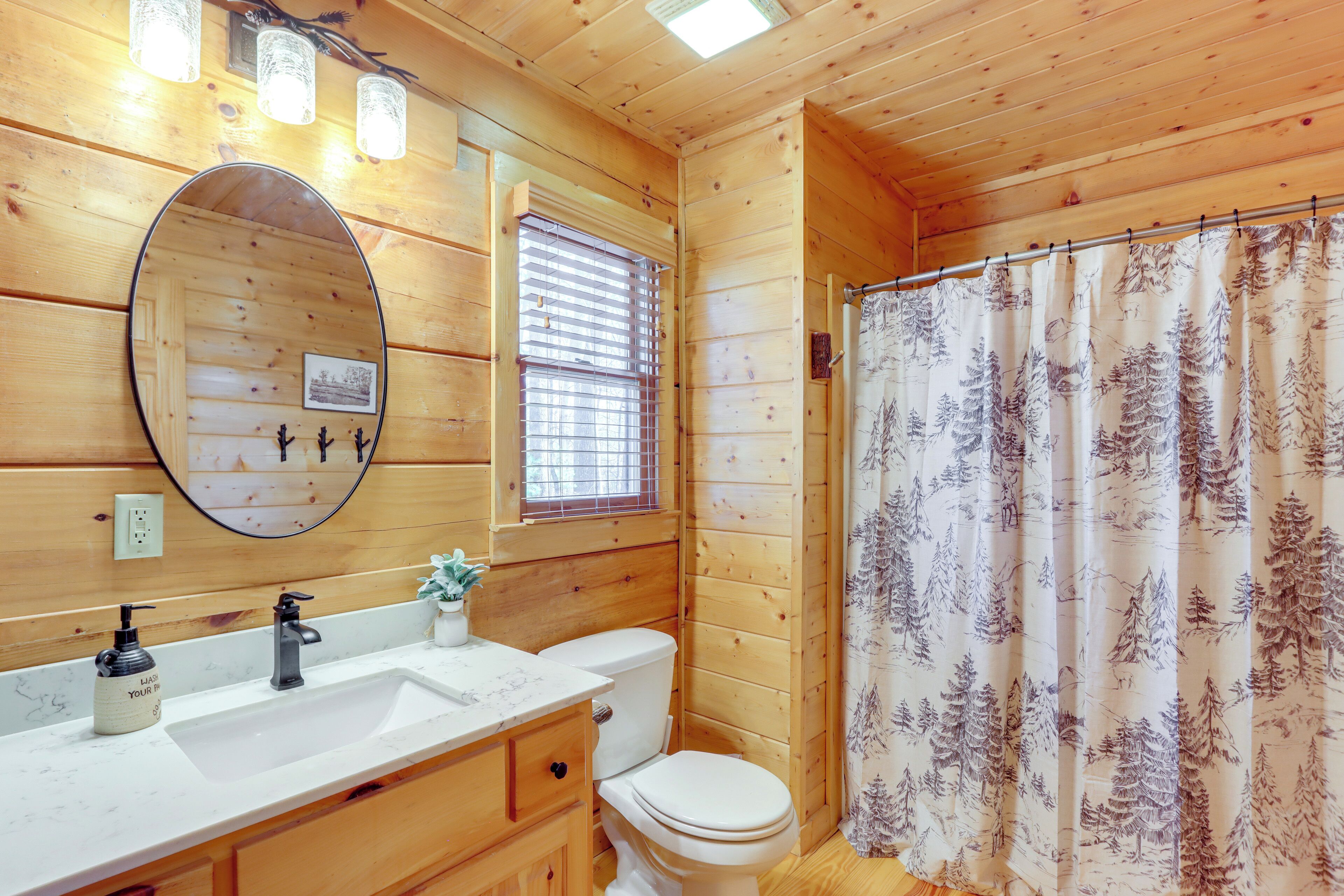 A wooden cabin bathroom with a sink, mirror, toilet, and shower curtain.