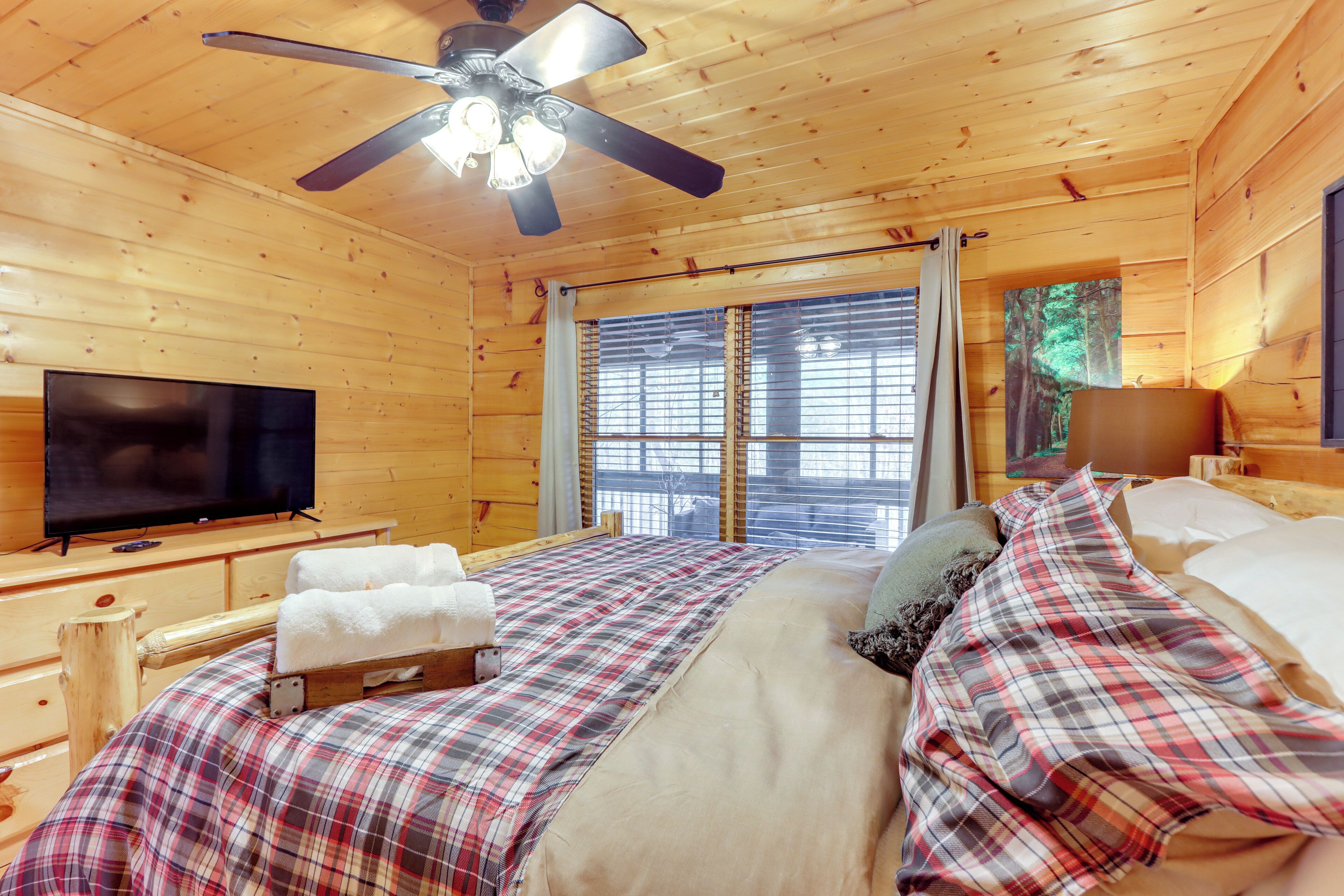 Ein Schlafzimmer einer Holzhütte mit einem Bett, einem Fernseher und einem Deckenventilator.