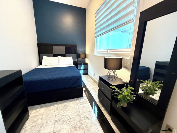 Un dormitorio con cama, mesita de noche, lámpara, cómoda, espejo y planta en maceta.