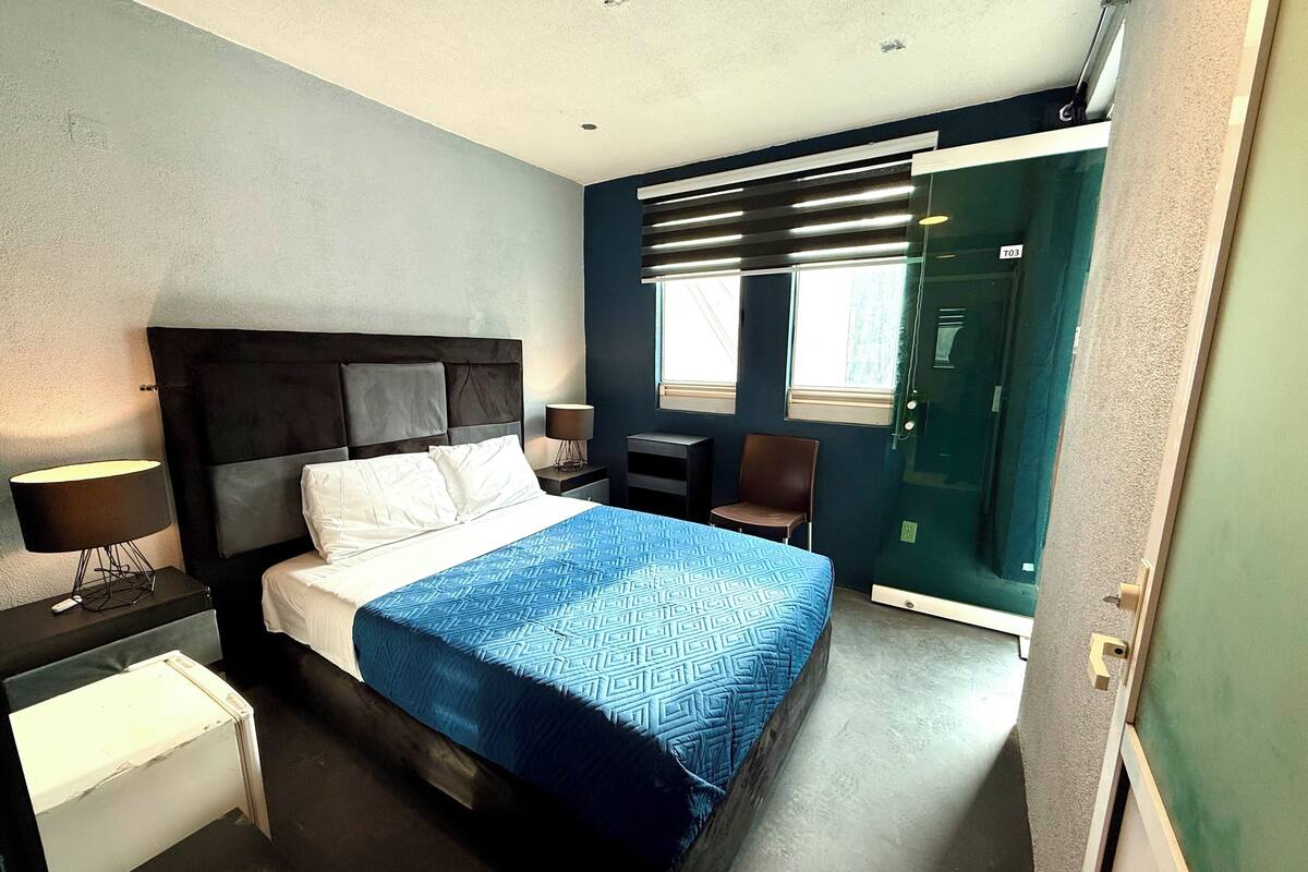 A hotel room with a bed, bedside tables, a chair, a desk, and a window.
