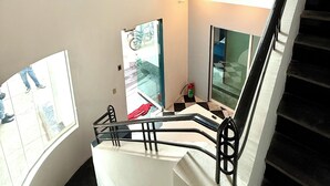 A multi-level interior with a staircase, glass railings, and a poster on the wall. - ROOMIES HOSTEL Reforma - La Diana (Mexico City)