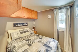 A bedroom with a bed, a wooden cabinet, a clock, and a window with curtains. - Fish, Hike & Relax: Riverfront Manistique Cabin (Manistique)