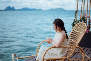 A person sitting on a wicker chair by a body of water, holding a cup. - Sand Bay Resort Semporna (Semporna)