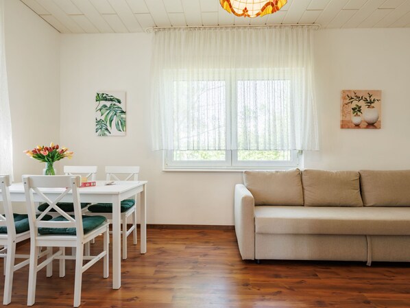 A dining area with a white table and chairs, a beige sofa, and a window with sheer curtains. - Green House by Interhome (Balatonmariafurdo)