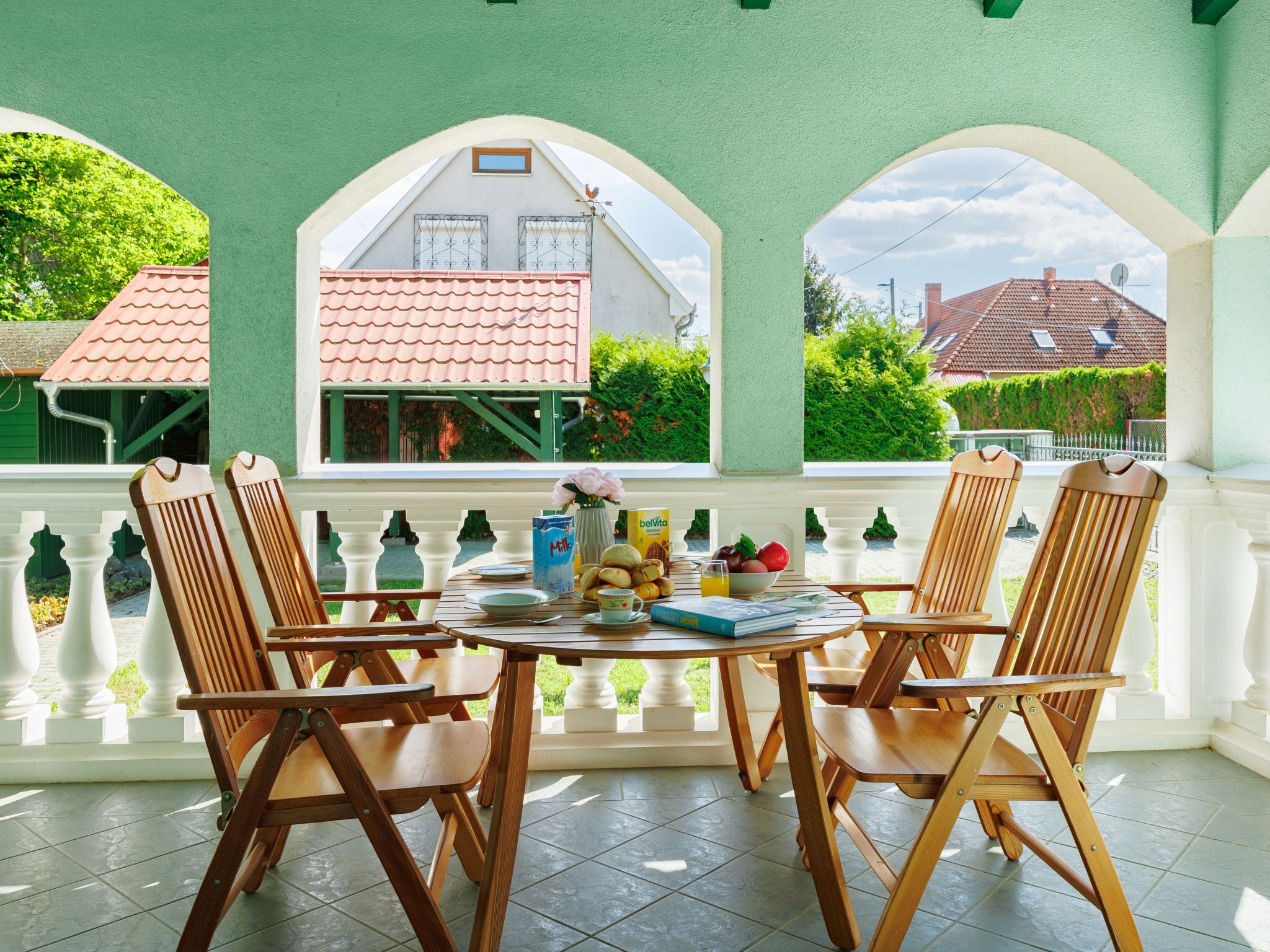 Une terrasse couverte avec quatre chaises en bois et une table préparée pour le petit-déjeuner.
