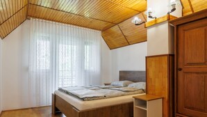A bedroom with a sloped ceiling, a wooden bed, a nightstand, a wardrobe, and a window with sheer curtains. - Green House by Interhome (Balatonmariafurdo)