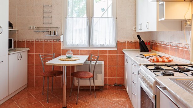 A compact kitchen with a dining table, chairs, a gas stove, and a window with curtains. - Green House by Interhome (Balatonmariafurdo)