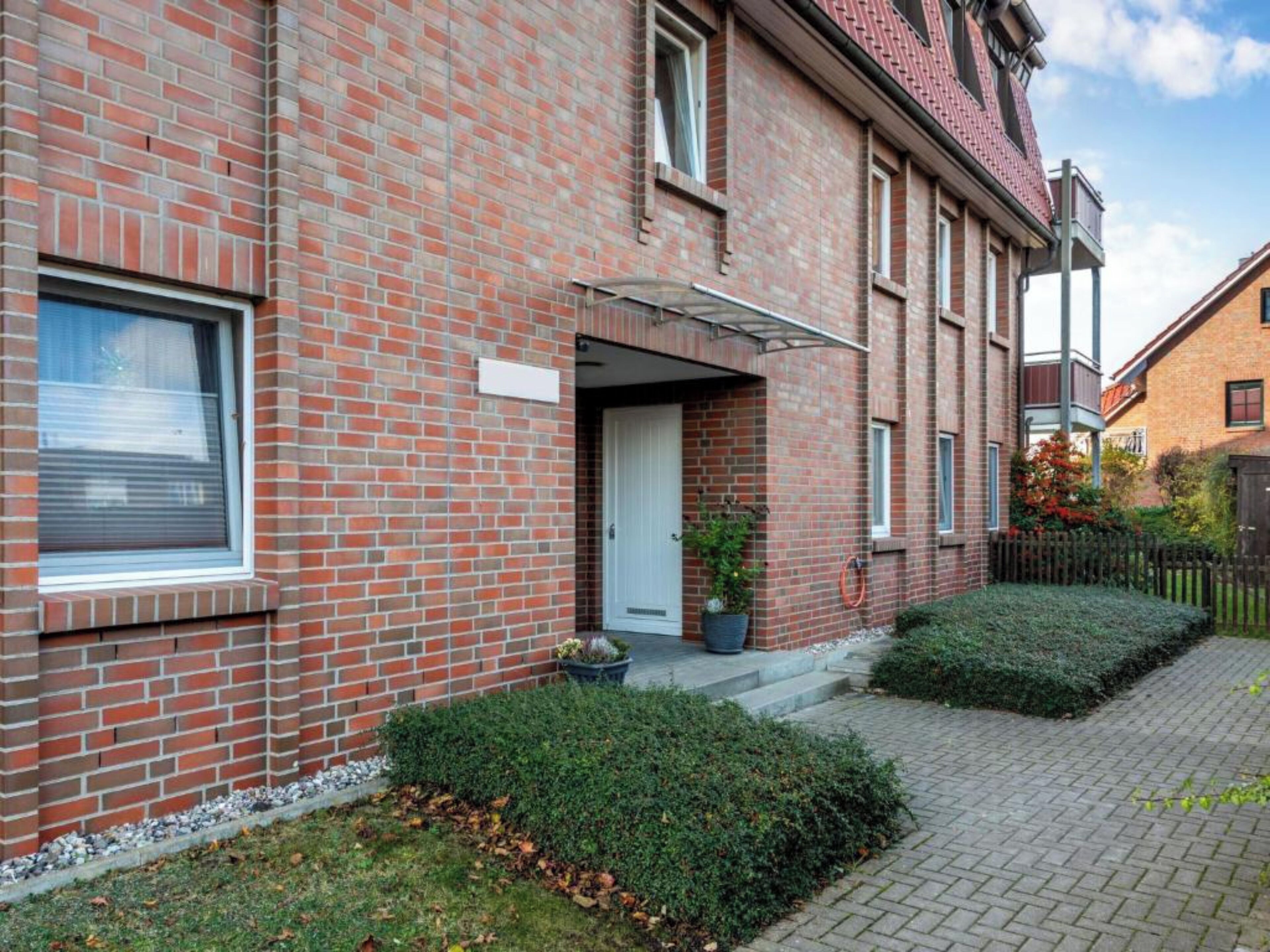Un bâtiment en briques rouges, avec une porte blanche et un petit porche.