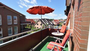 A balcony with a red umbrella, two lounge chairs, and a small table with a bottle.