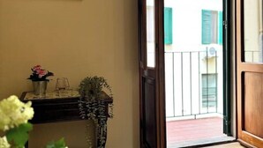 Een kamer met een houten deur die uitkomt op een balkon, een kleine tafel met een bloevas, en een spiegel aan de muur.