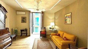 Een woonkamer met een bank, een houten kast, een lamp en uitzicht op buiten.