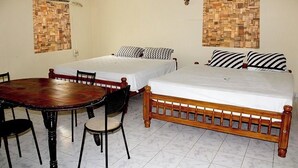 A room with two single beds, a wooden dining table with chairs, and a ceiling fan. - Corniche Inn Resorts (Anaikatti)