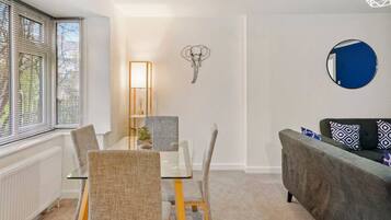 A modern living room with a dining table, chairs, a sofa, a wall-mounted mirror, and a decorative elephant head.