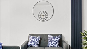 A modern living room with a grey sofa, two patterned throw pillows, a round wall clock, and a tall radiator. - Barnet EN5 - Elegant 2Bed/1Bath Ground Floor Flat with FREE WiFi (Greater London)