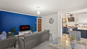 A modern living room with a grey sofa, a glass dining table, and a kitchen area with white cabinets and a built-in oven. - Barnet EN5 - Elegant 2Bed/1Bath Ground Floor Flat with FREE WiFi (Greater London)