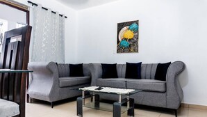 A living room with a grey sofa, a glass coffee table, and a wall-mounted abstract painting. - Villas Hillside apt 2 (Samaná)