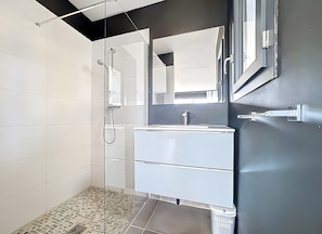 Une salle de bain moderne avec une douche à parois de verre, un meuble-lavabo blanc et un grand miroir.