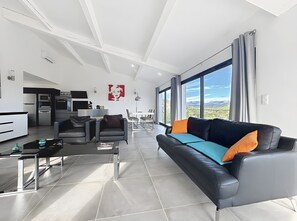 Uma sala de estar moderna com sofá, cadeiras, mesa de centro e cozinha ao fundo.