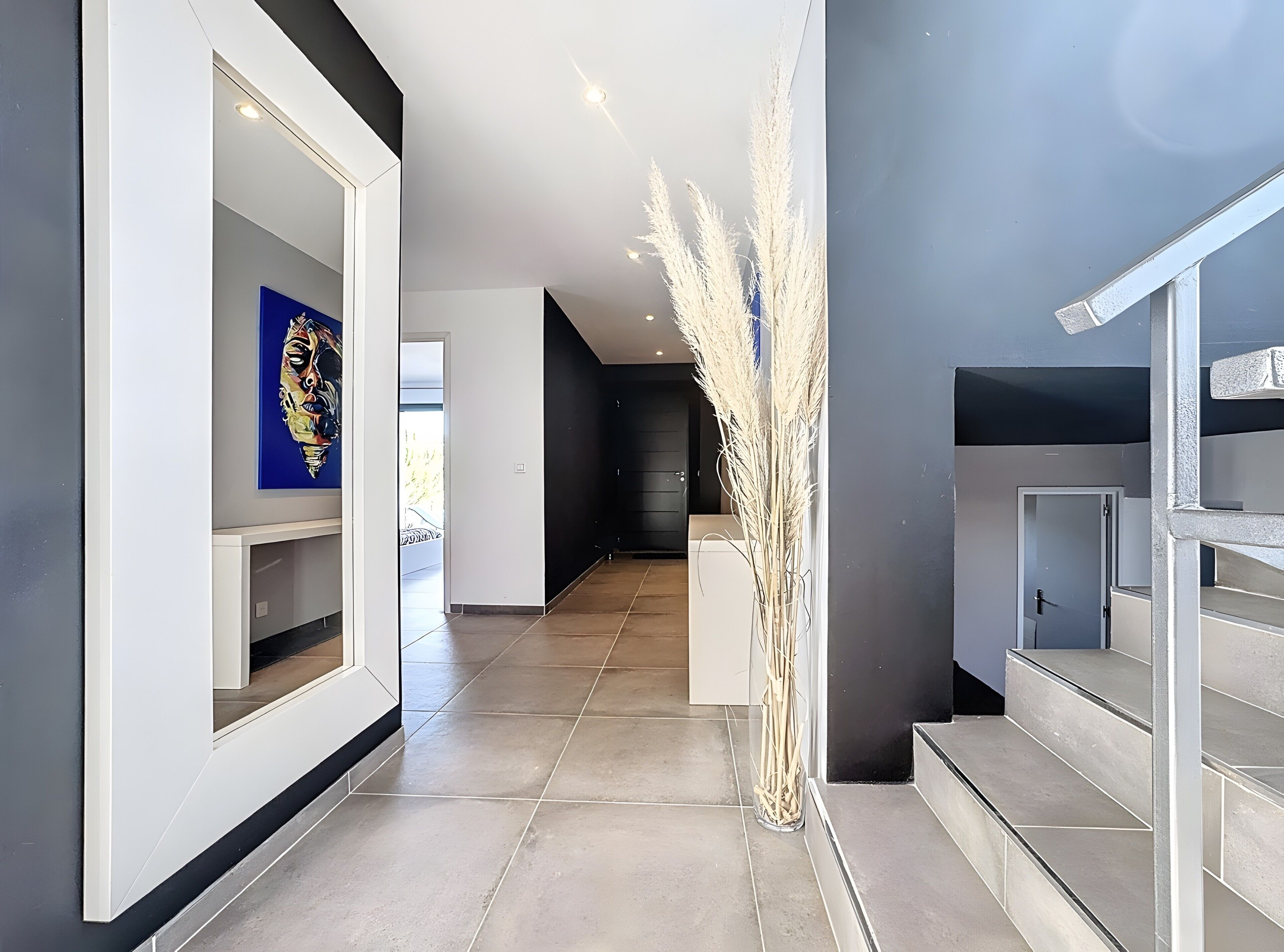 A modern hallway with a clear glass vase, a staircase, and a door leading to another room.
