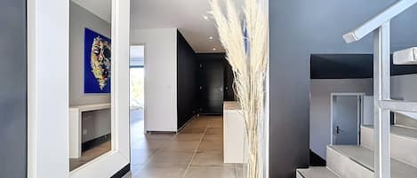 A modern hallway with a clear glass vase, a staircase, and a door leading to another room.