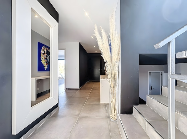 Un couloir moderne avec un vase en verre transparent, un escalier et une porte donnant sur une autre pièce.