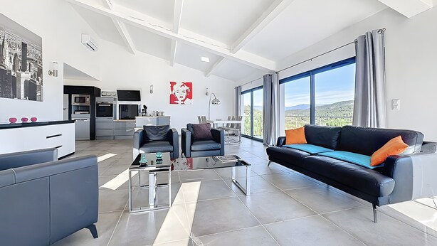 A modern living room with a sofa, chairs, a coffee table, and a kitchen in the background.