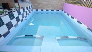 En swimmingpool med ett rutmönstrat kantparti, omgiven av ett rosa staket och en stenmur.