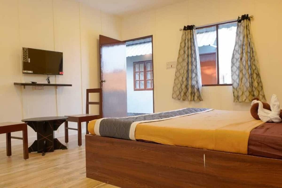A bedroom with a wooden bed, a TV on a shelf, a desk, and a window with curtains.