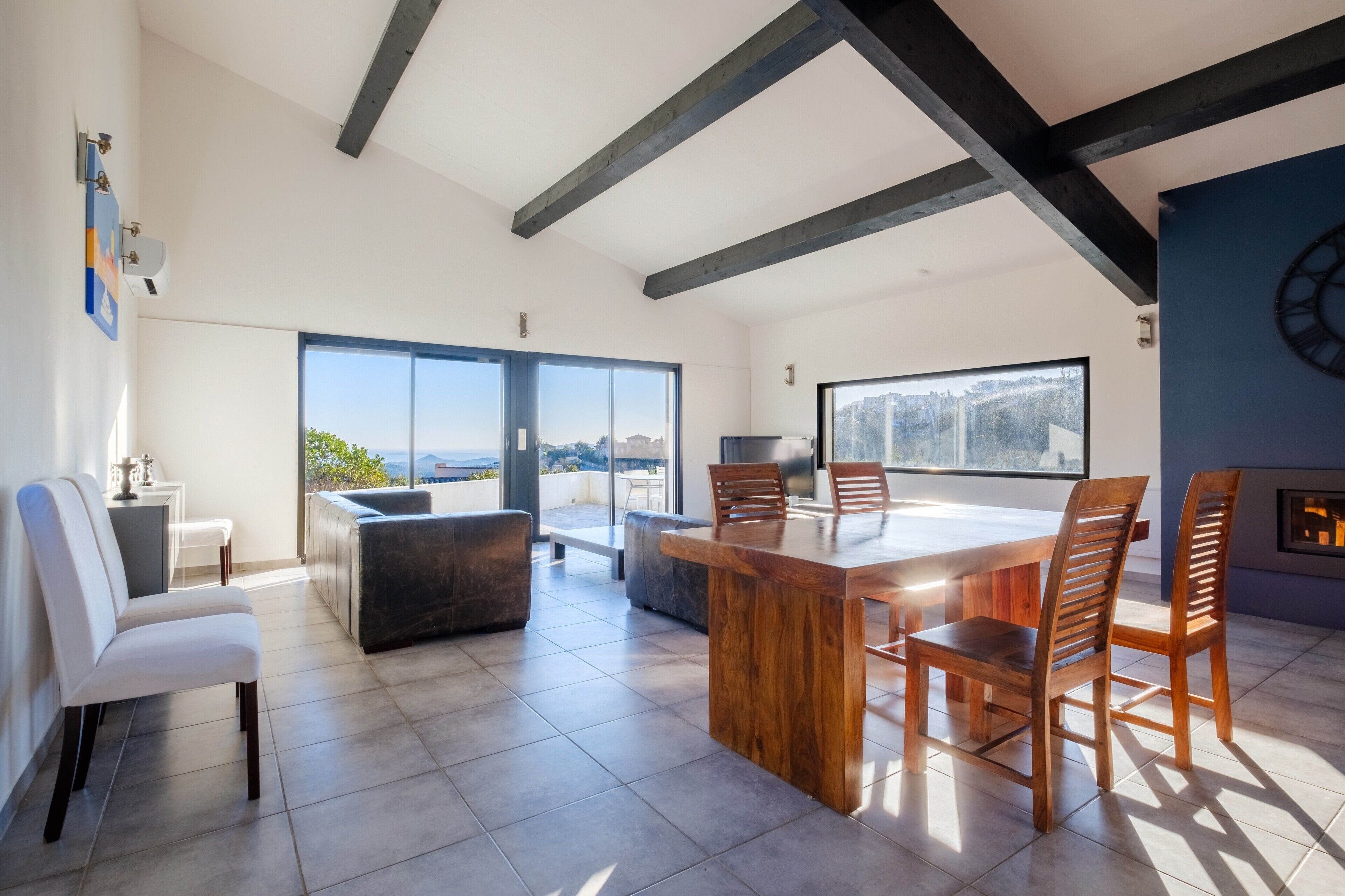 A modern dining area with a wooden table and chairs, large windows, and a view of the city.