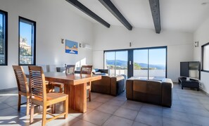 Un vaste espace de vie comprenant une table à manger en bois, des sièges confortables, de grandes fenêtres et une vue sur l’extérieur.