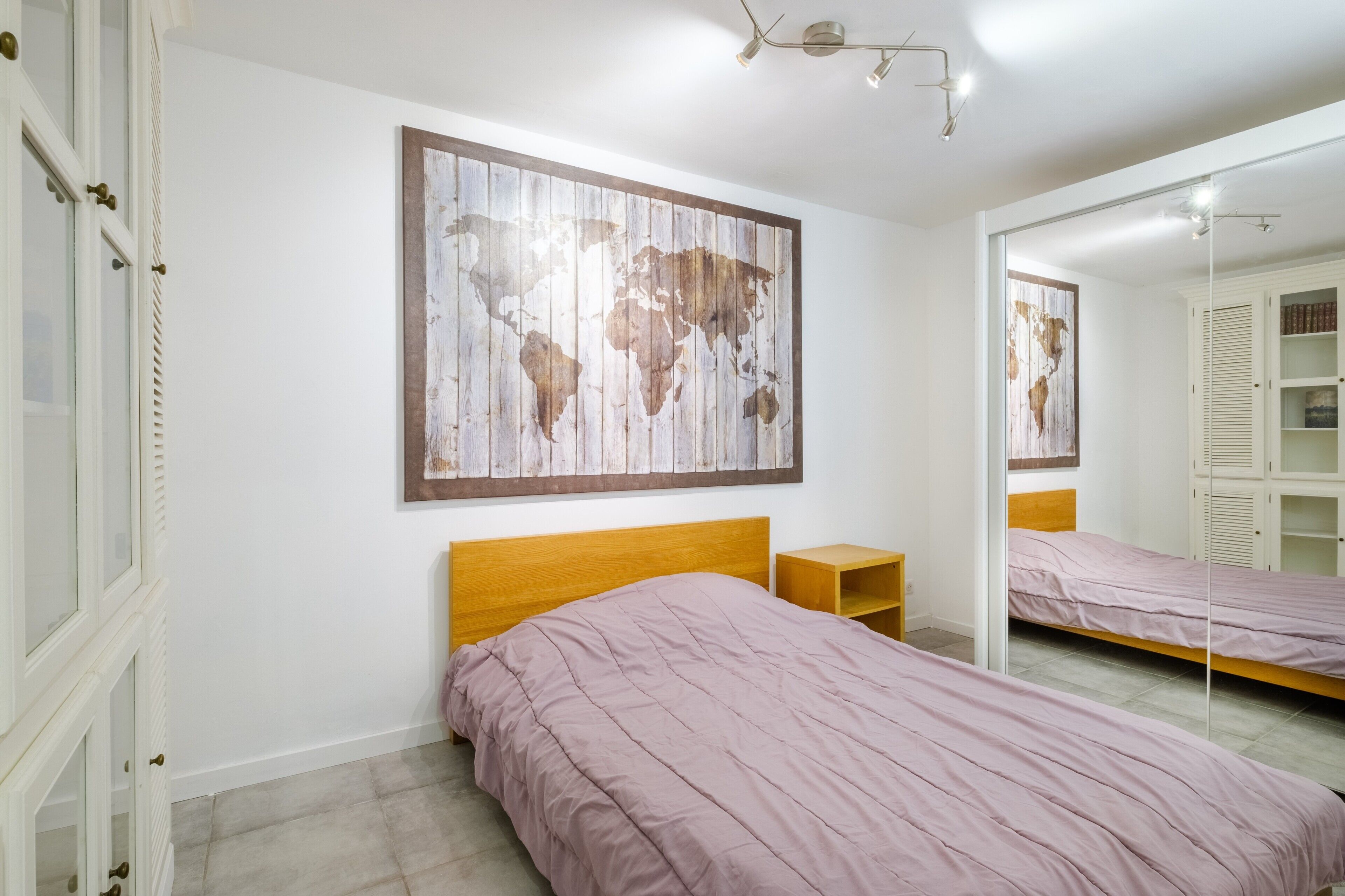 Un dormitorio con una cama, una mesita de noche, un armario y un mapa del mundo en la pared.