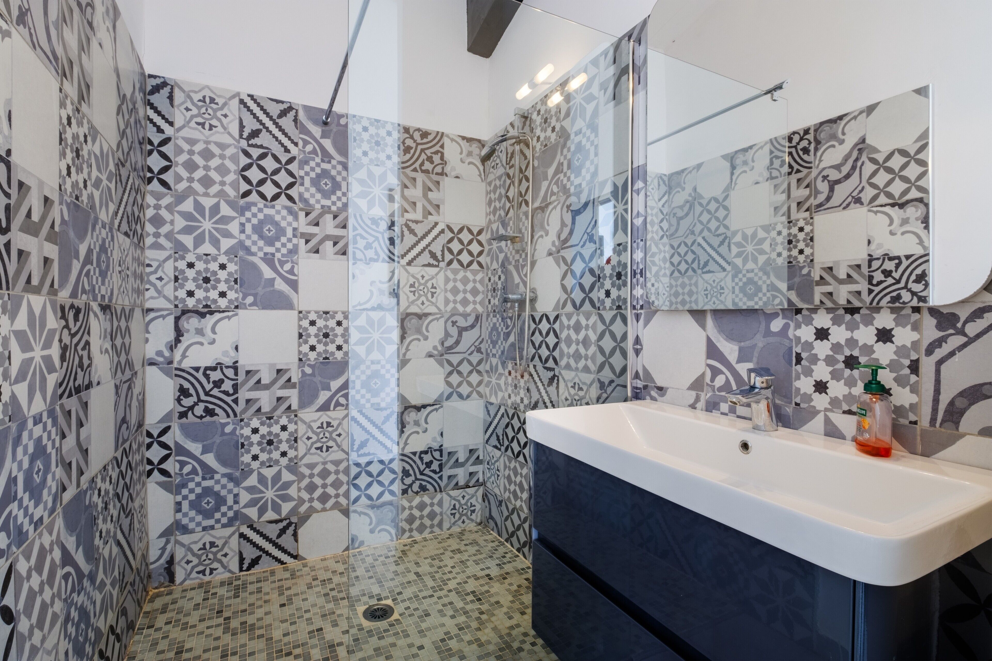 Un bagno con piastrelle decorative, box doccia in vetro, lavabo con specchio e dispenser di sapone.