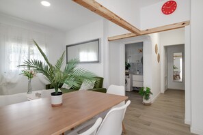 A dining area with a wooden table, white chairs, and potted plants.
