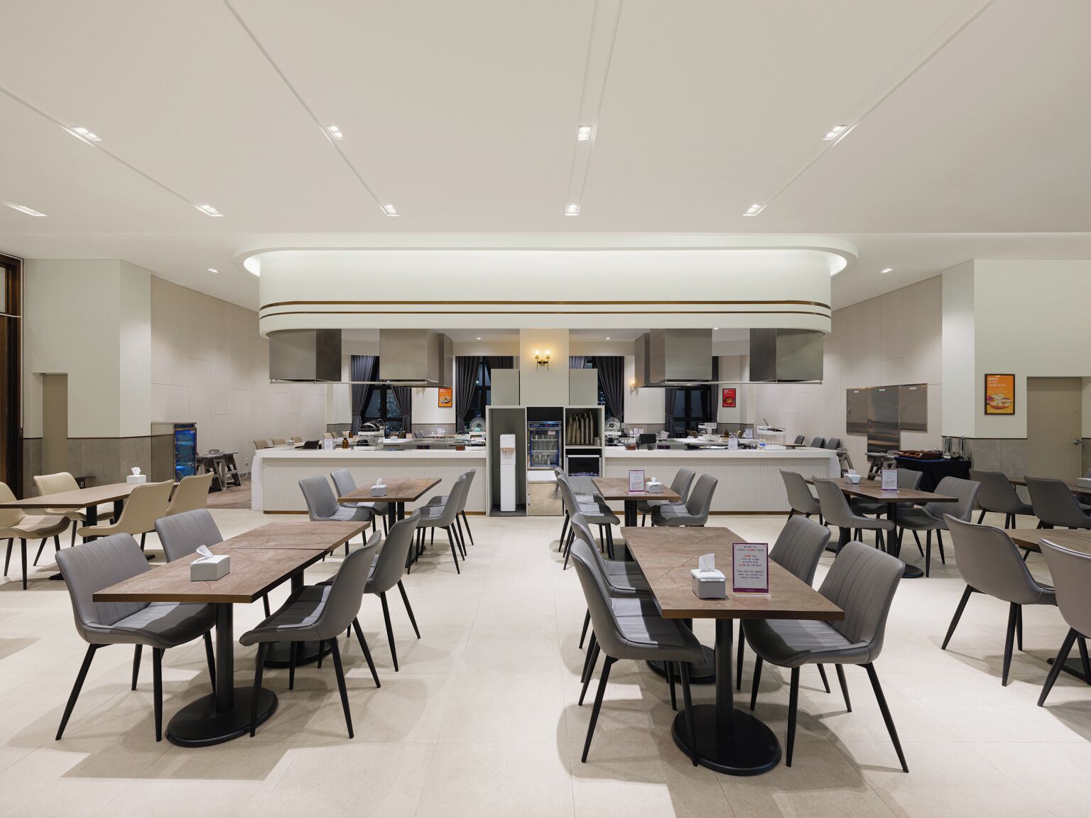 A modern dining area with multiple tables and chairs, a central kitchen area, and a clean, minimalist design.