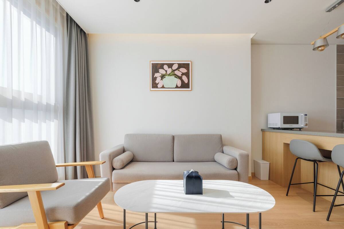 A modern living room with a sofa, a round coffee table, and a kitchen area with a microwave.