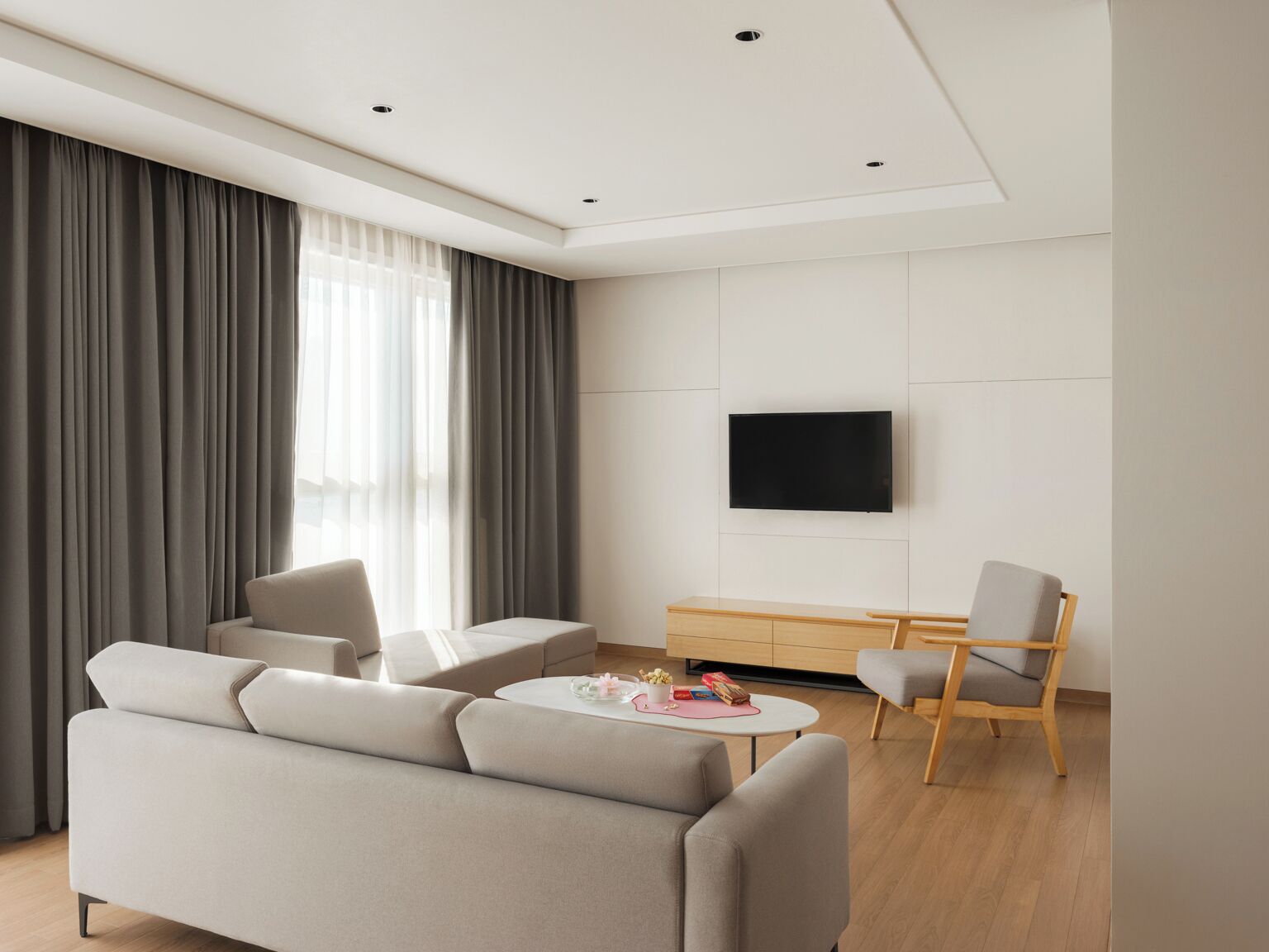 Una sala de estar moderna con un sofá, una mesa de centro, un televisor montado en la pared y un mueble de madera.