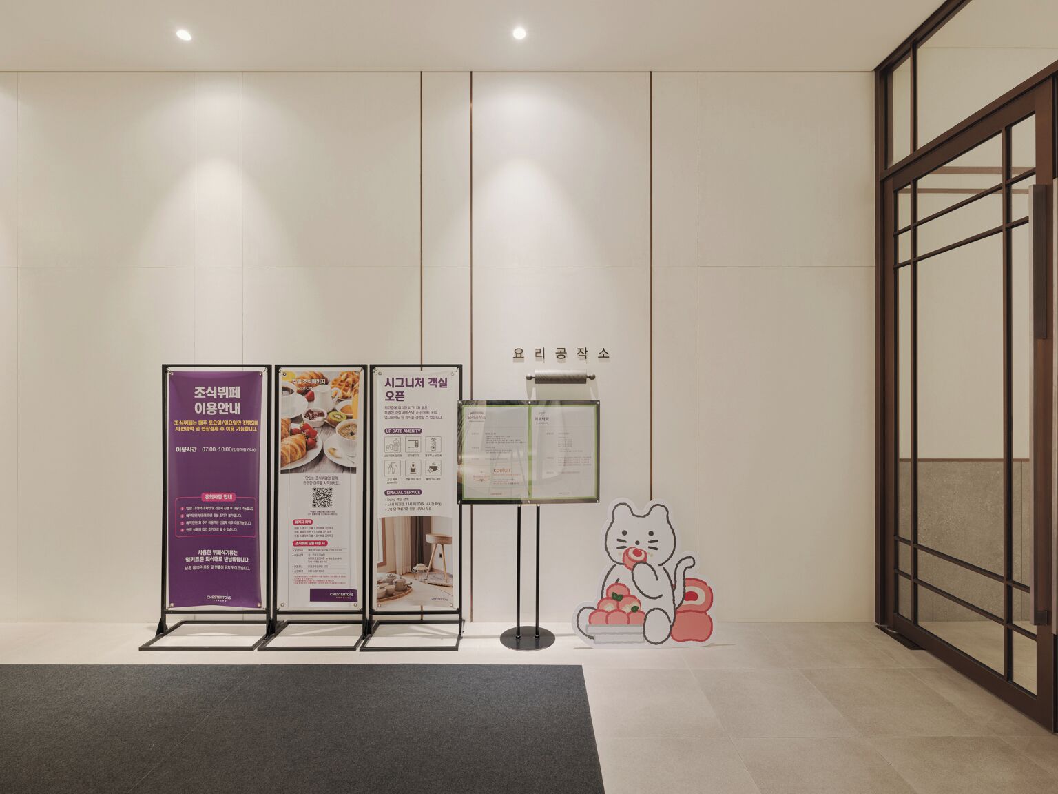 A clean, modern interior with a reception area featuring a cat decoration, informational posters, and a signboard.