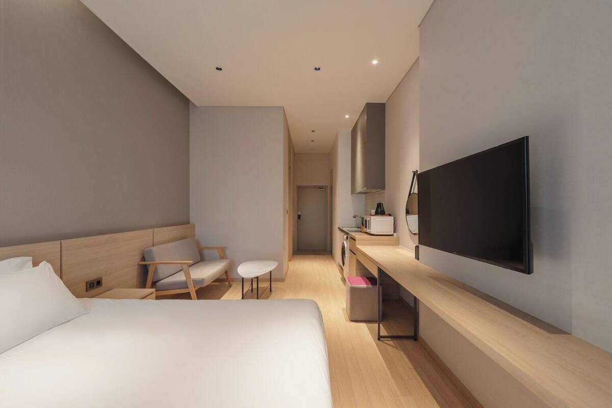 A modern hotel room with a large bed, a desk with a flat-screen TV, a chair, and a small table.