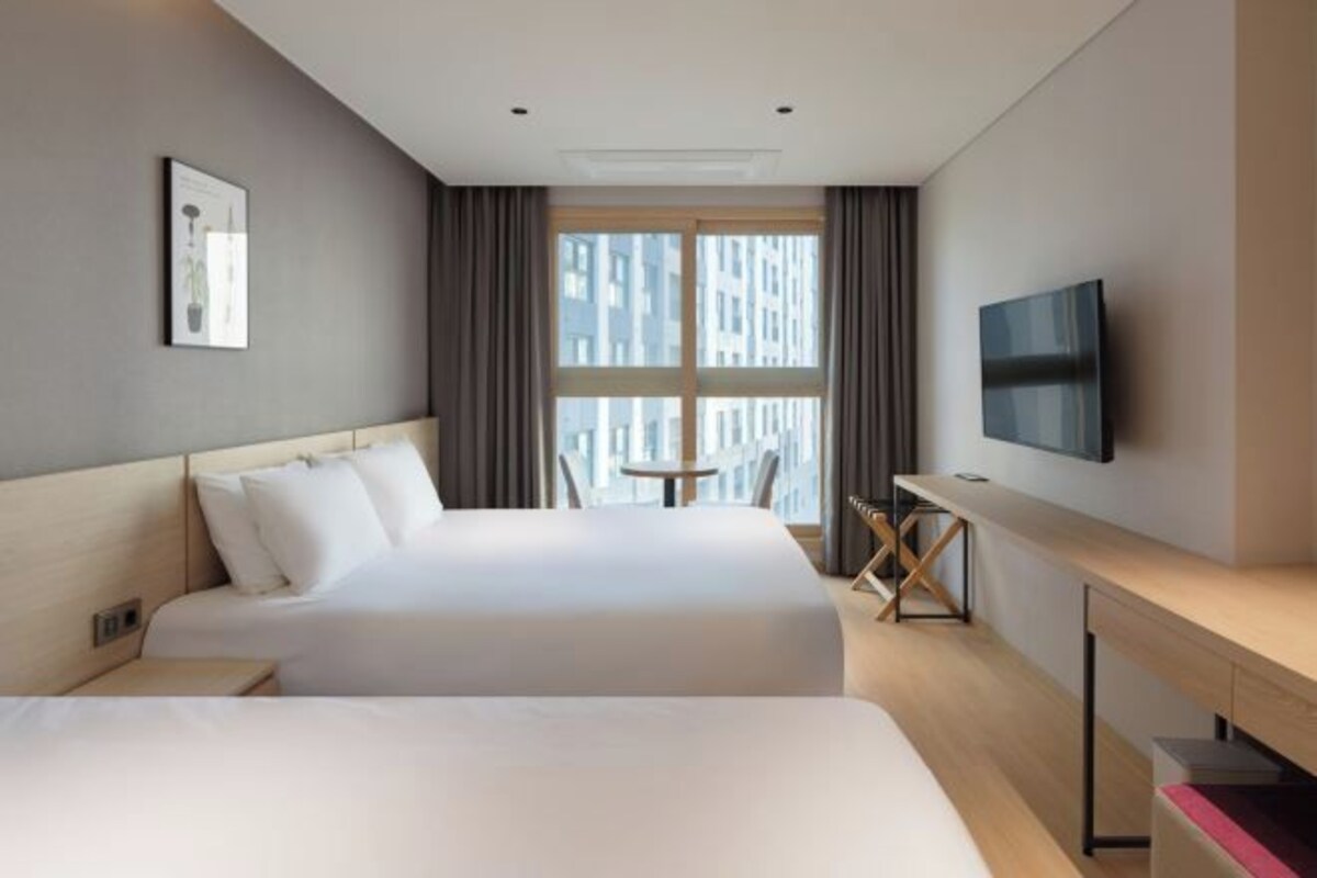 A hotel room with two beds, a desk, a TV, and a window with curtains.