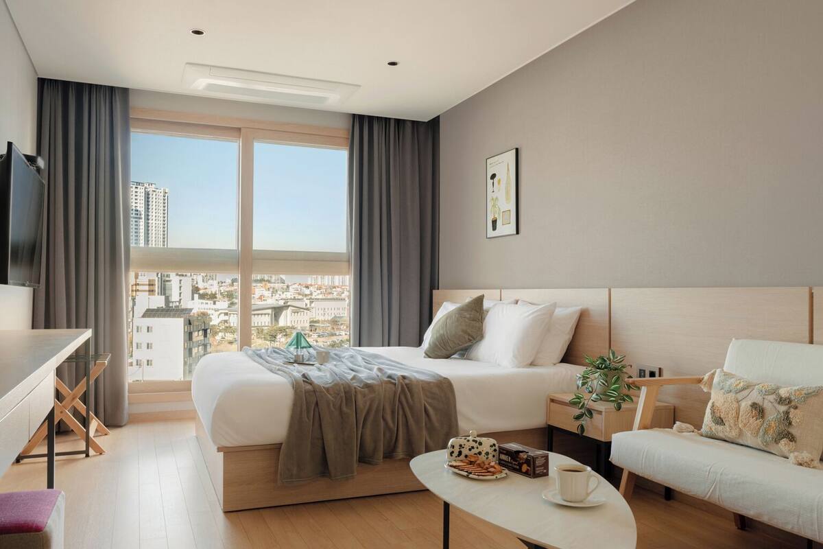 A modern hotel room with a large bed, a sofa, a small table, and a desk.