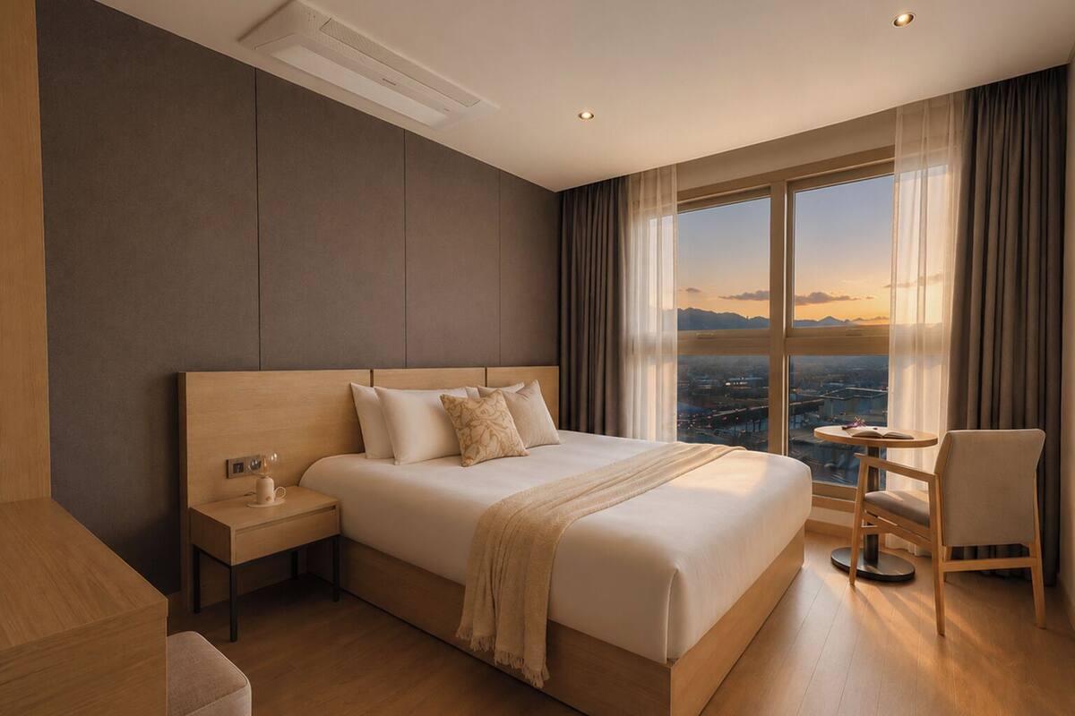 A modern hotel room with a large bed, a bedside table, a chair, and a view of the cityscape.