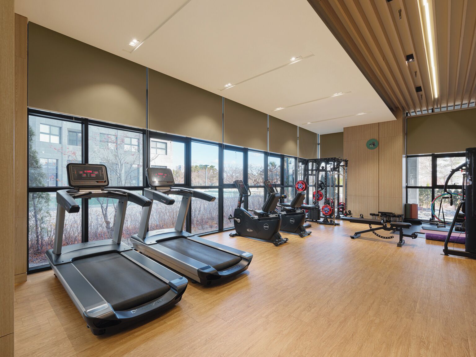Un gimnasio moderno con cintas de correr, máquinas de pesas y un amplio ventanal con vistas al exterior.