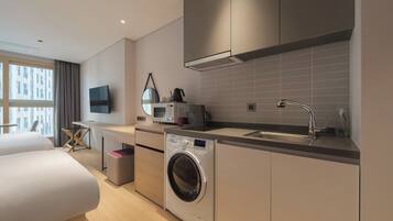 Una habitación de hotel moderna con una cama, lavadora, kitchenette y un gran ventanal.