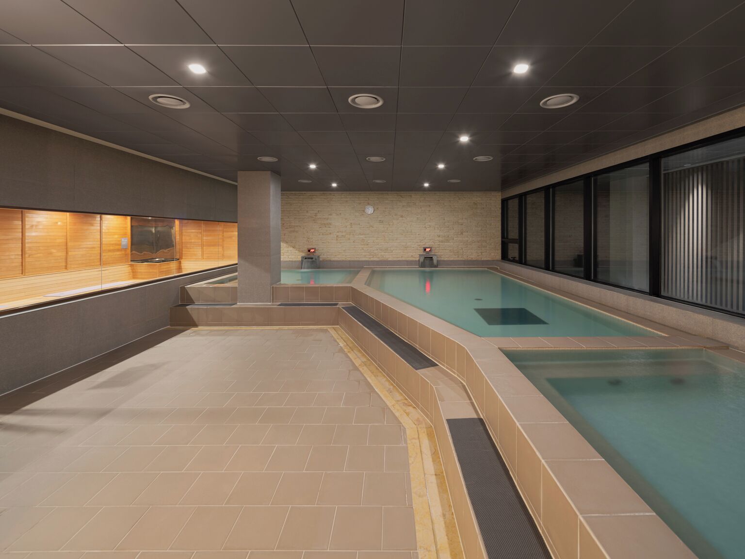 A modern indoor swimming pool with a wooden bench area and a spa section.