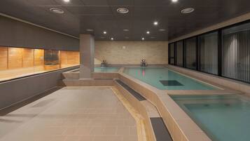 Una piscina interior moderna con zona de bancos de madera y sección de spa.