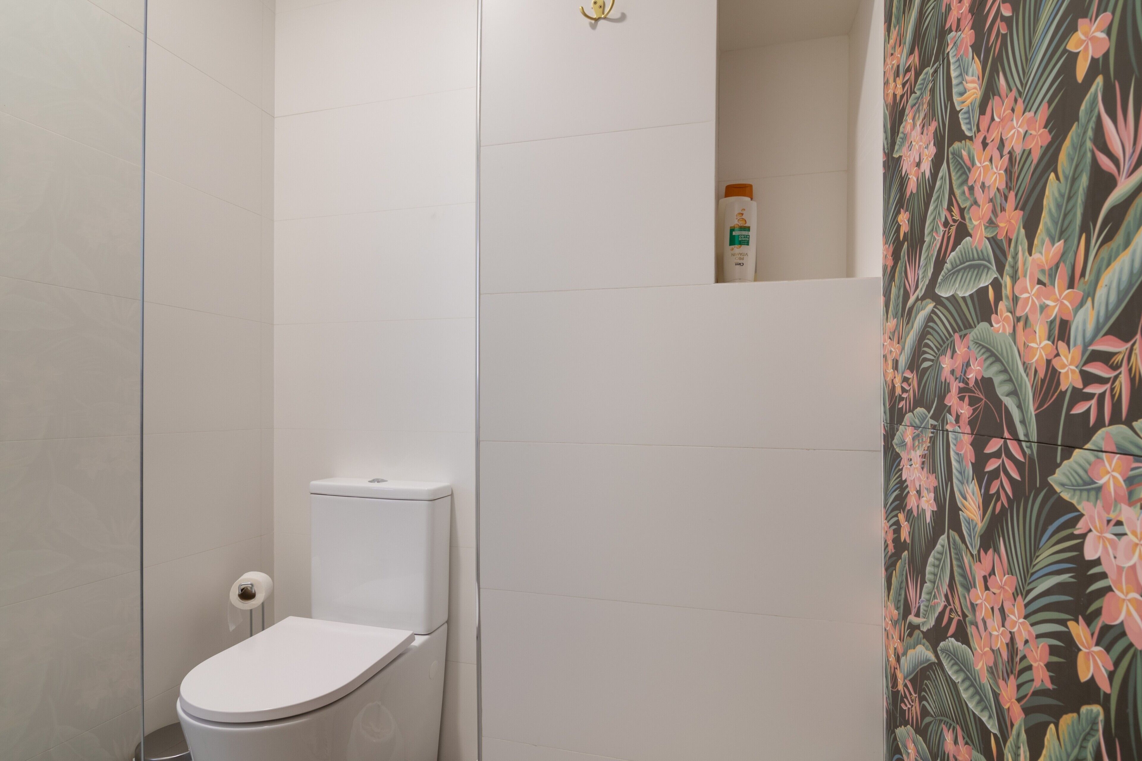 Een badkamer met toilet, douchegedeelte en een wand met bloemenprint.