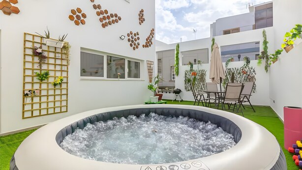 A modern outdoor space with a hot tub, a wooden lattice wall with plants, and a dining area with chairs and a table.