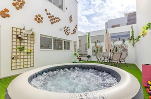 Un espace extérieur moderne doté d’un jacuzzi, d’un mur en treillis de bois orné de plantes et d’un coin repas avec des chaises et une table.